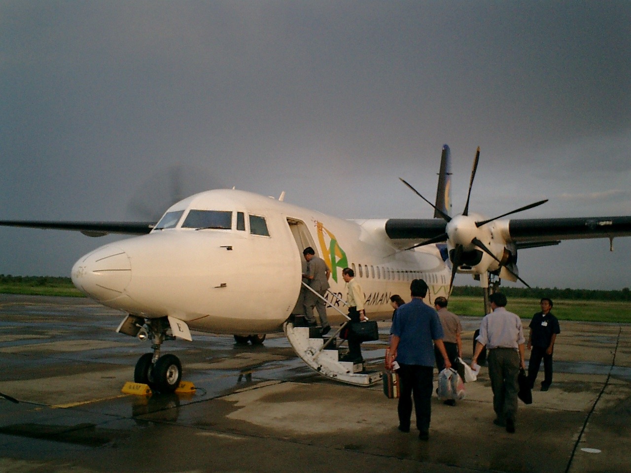 雨上がりの駐機場でプロペラ機へ搭乗する人々